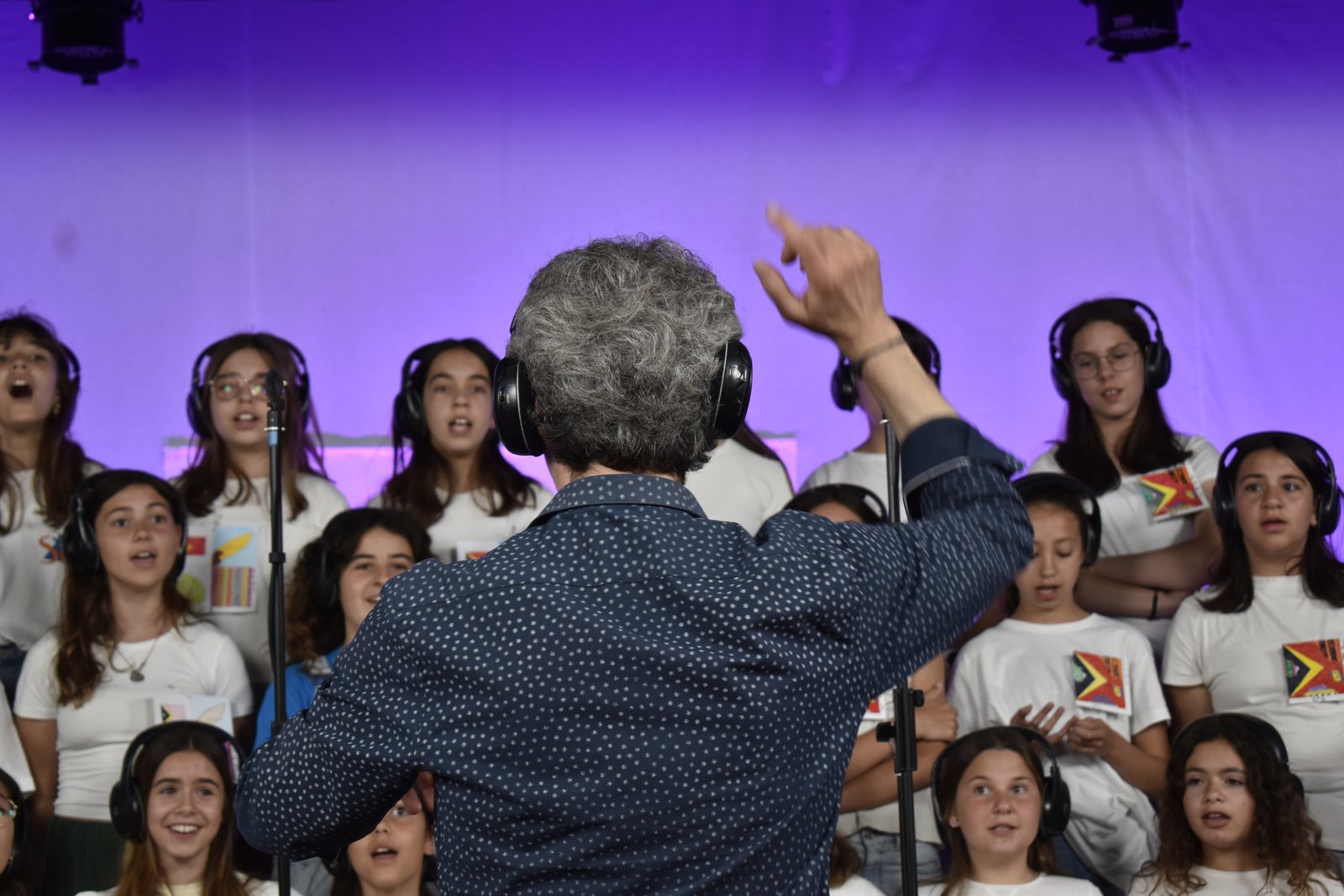O maestro a dirigir o coro sob luz roxa, na gravação